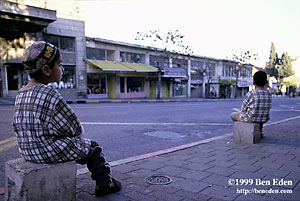 Two small Arab (or Jewish?) boys, one of them with an embroided hat, both wearing  identical traditional shirts sit on cornerstones along the Jaffa (Yaffo) Street in Jerusalem, Israel