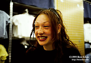 A teenage redhair freckled salesgirl with a pierced nose wearing a headset microphone smiles at a customer in a clothing store in a Mall in New York City, USA
