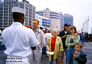 A black Unites States Navy sailor directs visitors waiting in line to board the USS Intrepid Aircraft Carrier Museum on a Memorial Day in Manhattan, New York