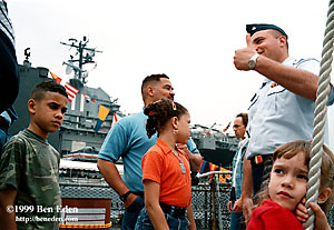 A Unites States Navy sailor gives a hands-up sign to a hispanic family touring a US Coast Guard boat moored next to the USS Intrepid Aircraft Carrier Museum on a Memorial Day in Manhattan, New York