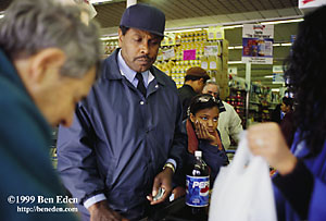 A black teenage girl leans on the cash register conveyor belt, waiting for her turn next to a Pepsi bottle in a Queens, New York, K-Food supermarket