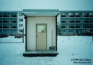 A balding, middle-aged male  security guard sits inside his flourescent-lit cubicle surrounded by snow at a Coca-Cola warehouse inOlomouc, Czech Republic