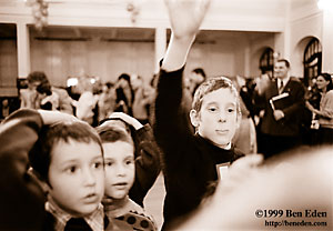 A Prague Jewish boy lifts his hand to answer a Chanukah (Hanukah) quiz question while two smaller boys stand by dazzled. 