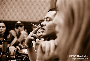 An attractive Jewish young man wearing silver jewellery holds a cigarette theatrically while he's smoking at a table at a Chanukah (Hanukah) celebration held in Prague, Czech Republic Jewish Community's eating hall.
