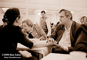 Older Jewish man in a white kippa holds the hand of his daughter across the table at a Chanukah (Hanukah) celebration held in Prague, Czech Republic Jewish Community's eating hall.