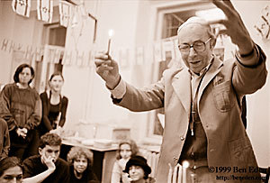 A Czech Jewish Holocaust survivor lights up the Chanukiah (Hanukiah, Menorah) in celebration of Chanukah (Hanukah) at Prague Hebrew Ulpan while students watch and Israeli flags hang around.