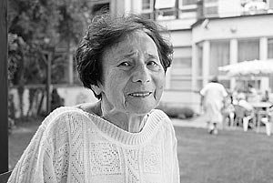 Sarlota Kralova, a Czech Jewish Holocaust survivor wearing a hand-knitted white sweather, walking in the garden of the Charles Jordan retirement home in Prague and smiling.