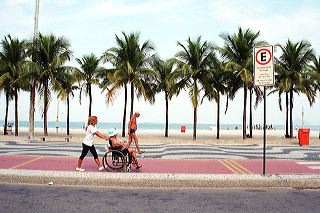 An invalide is being pushed on a wheelchair along Rio de Janeiro's Copacabana beach as a brazilian senior jogs by
